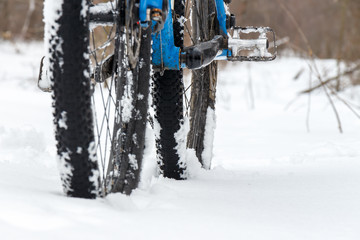 A bicycle standing in the snow close up. Snow flakes floating on dark off-road tires. Winter weather in the field.