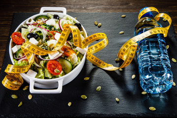 Bottle of water with vegetable salad on plate on wooden table