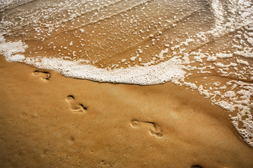 wave covers footsteps on the beach