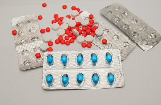 Great number of the spilled red and white pills, and also packing of blue pills