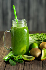 Blended green smoothie with ingredients on wooden table selective focus