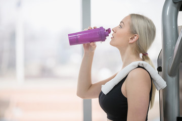 Young sexy woman drinking water and taking a break after workout in gym