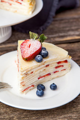 Crepe cake bakery piece with strawberry and vanilla sauce on wood table. Maslenitsa, traditional Russian holiday