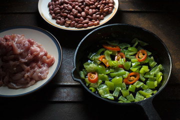 Pieces of chicken, beans. Pepper and chili in a frying pan.