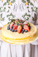 Female hands holding crepes cake with strawberry and vanilla sauce.