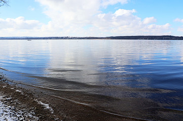 Ammersee Bavarian lake idyllic winter view, shore covered by snow and blue sky reflecting on the calm water surface