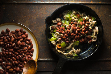 Beans are spread in a frying pan with pepper and chicken.