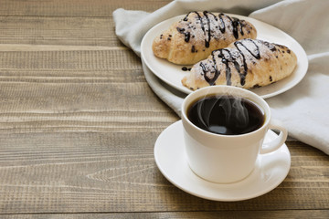 Two freshly baked chocolate croissants and cup of coffee on wooden board. Breakfast concept.
