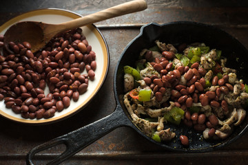 Beans are spread in a frying pan with pepper and chicken side view