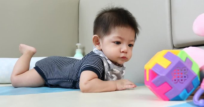 cute asian baby boy playing ball toy on soft mattress floor in nursery room