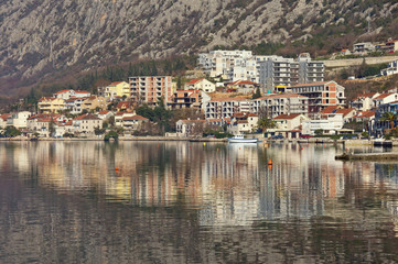 Fototapeta na wymiar Residential area of Dobrota town, located at the foot of the mountain, is reflected in the water. Montenegro, Bay of Kotor