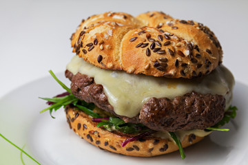 Rustic home made cheesburger with melting cheese and with dijonnaise sauce on white table on white background