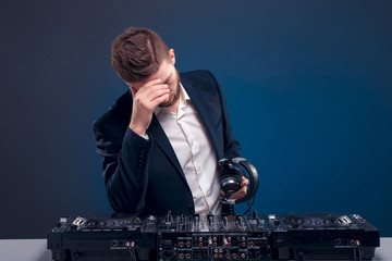 Man DJ in dark suit play music on a Dj's mixer. Studio shot. Dark blue background. Sad of something...