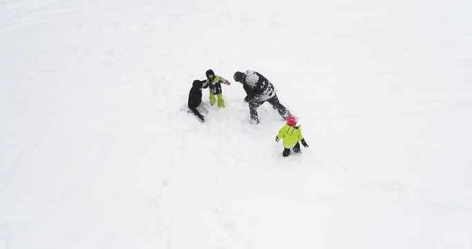 Orbit aerial over  father,mother, two children lying playing and hugging on white covered winter snowy field.Family people together enjoy childhood and have fun outdoors.4k straight-down perspective