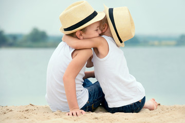 Two brothers relaxing on the beach of the lake.The little boy tenderly embraces his older brother.	