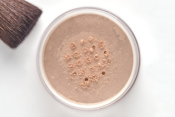 Cosmetic powder for face in jar and brush on white background.