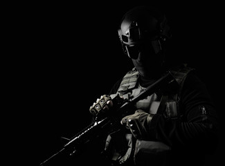 Black and white photo of equipped swat soldier standing with rifle on black background.