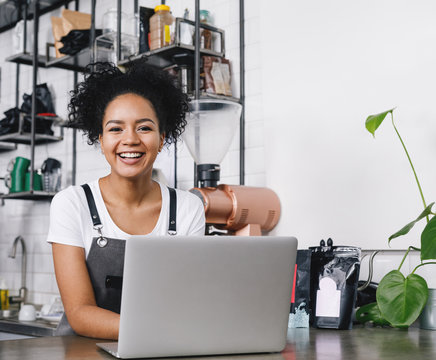 Happy business owner standing at counter with her laptop