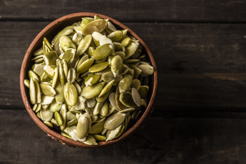 Pumpkin seeds in a clay plate on wooden old boards.