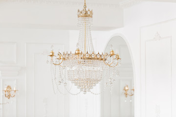 Expensive interior. Large electric chandelier made of transparent glass beads. White ceiling decorated with stucco molding. White patterned. Mouldings element from gypsum.