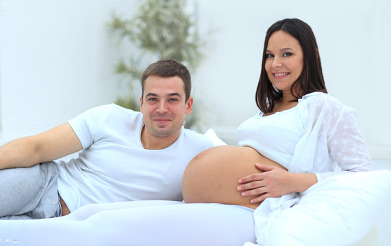 Laughing caucasian pregnant woman lying on bed with her husband in the bedroom