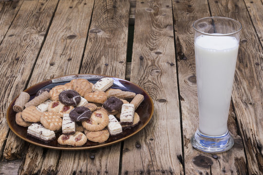 Vaso con leche, plato con galletas y pastas, sobre mesa de madera rustica