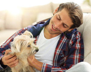 handsome guy stroking his dog while sitting in a large armchair.