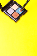 Brush for make-up over a set of eye shadow on yellow background. Copy space