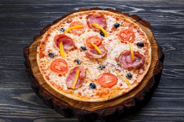 Delicious sicilian pizza with bacon, olives and tomatoes served on chopped wood. Italian food, restaurant or pizzeria concept