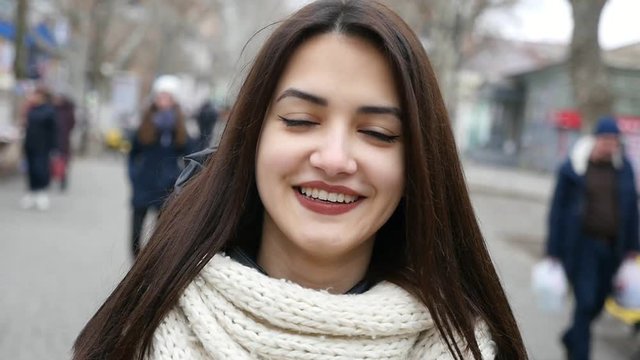    An amazing view of a beautiful girl with long loose hair who strolls in a city street and smiles open-heartedly in winter in slow motion