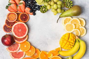 Healthy eating, top view of healthy fruits in rainbow colours in a frame, strawberries, mango, grapes, bananas, grapefruit on the off white table, copy space for text in the middle, selective focus