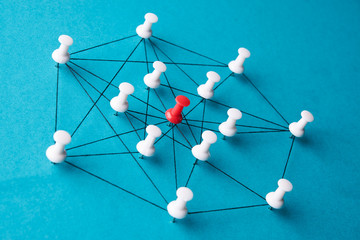 Network connection made from push pins and thread on blue background, close-up. Pin needles...