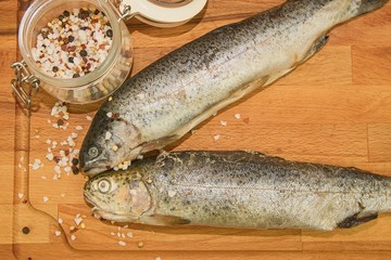 Two raw rainbow trouts with spices on wooden board. Healthy food and dieting concept. Close-up