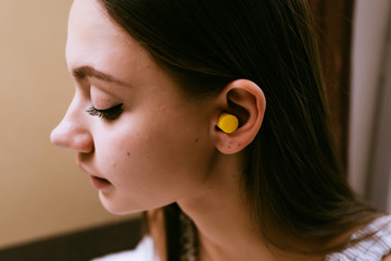 cute young girl wants to sleep, put in the ears of yellow earplugs against street noise