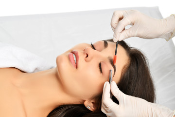 Fototapeta premium Beautician doing permanent eyebrows makeup. Closeup composition of beautiful woman face with thick brows In beauty salon