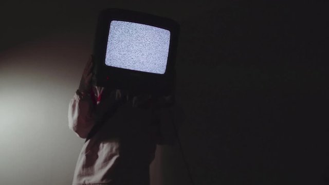 Young caucasian punk man pick up television set working static screen puts it in front of face in dark room