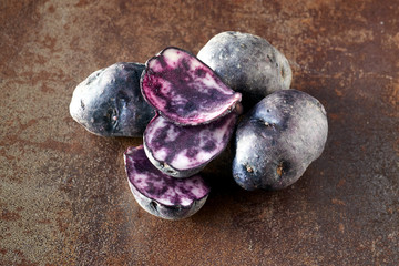 Sliced vitelotte potatos, three slices and three whole potatos on dark