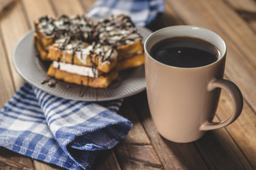 waffles with cream and chocolate on the plate and coffee on a wooden table.