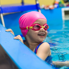 A little girl of European appearance in glasses in the pool, smiling and looking at camera