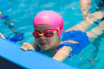 Fototapeta na wymiar A little girl of European appearance in glasses in the pool, shows the language and looking at the camera
