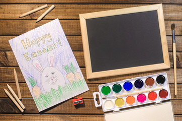 A child's drawing on the theme of Easter: egg, Bunny, congratulation with Easter. The view from the top, paints, pencils, brush and pattern. Free space for text.