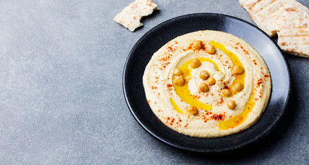 Hummus, chickpea dip, with spices in a black plate on grey stone background. Top view. Copy space.