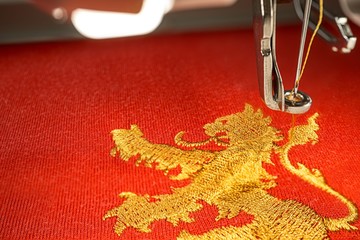 Close up picture of embroidery machine and gold lion design - Powered by Adobe