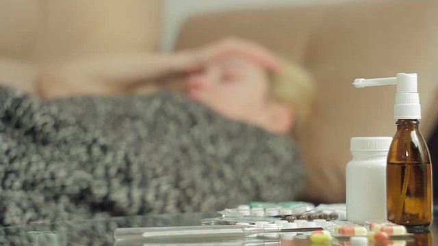 An adult woman with symptoms of illness lies on the couch under the blanket cover.