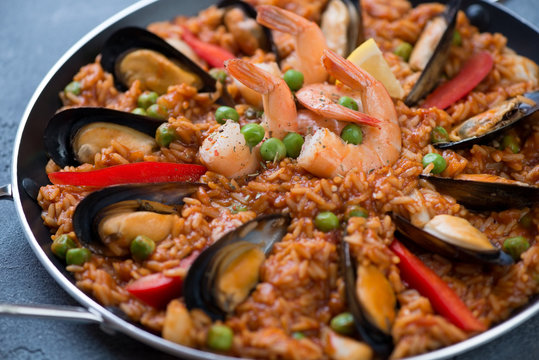 Close-up of spanish paella with mussels, tiger shrimps, calamari, green peas and red bell peppers slices, selective focus