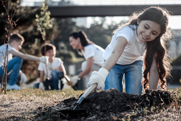 Young enthusiast. Nice pretty delighted girl holding a rake and using it while planting the tree