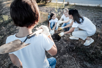 Fototapeta premium Gardening tools. Selective focus of a spade being held by a nice cute positive boy while working with his team