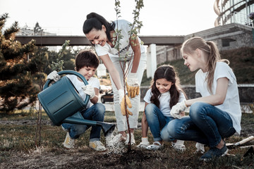 Grow strong. Cute positive nice boy holding a watering pot and watering a tree while making Earth a...