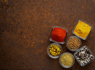 Mix spices on a dark brown rusty metal table - coriander seeds, ground red pepper, salt, black pepper, rosemary, turmeric, curry, coriander. Top view, empty space.
