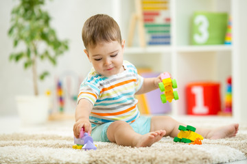 Happy child playing with colorful plastic bricks on the floor. Toddler having fun and building a train out of constructor bricks. Early learning. Developing toys